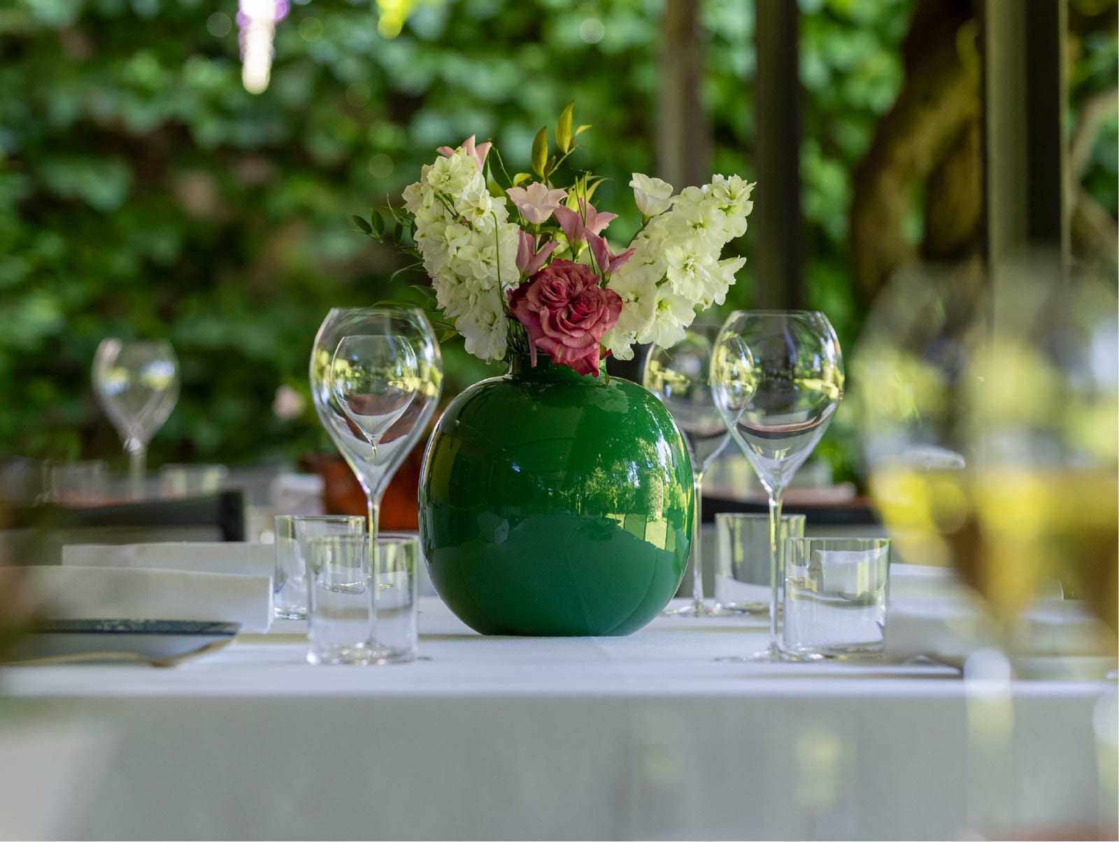 Tavolo apparecchiato all’aperto con un vaso verde di fiori freschi