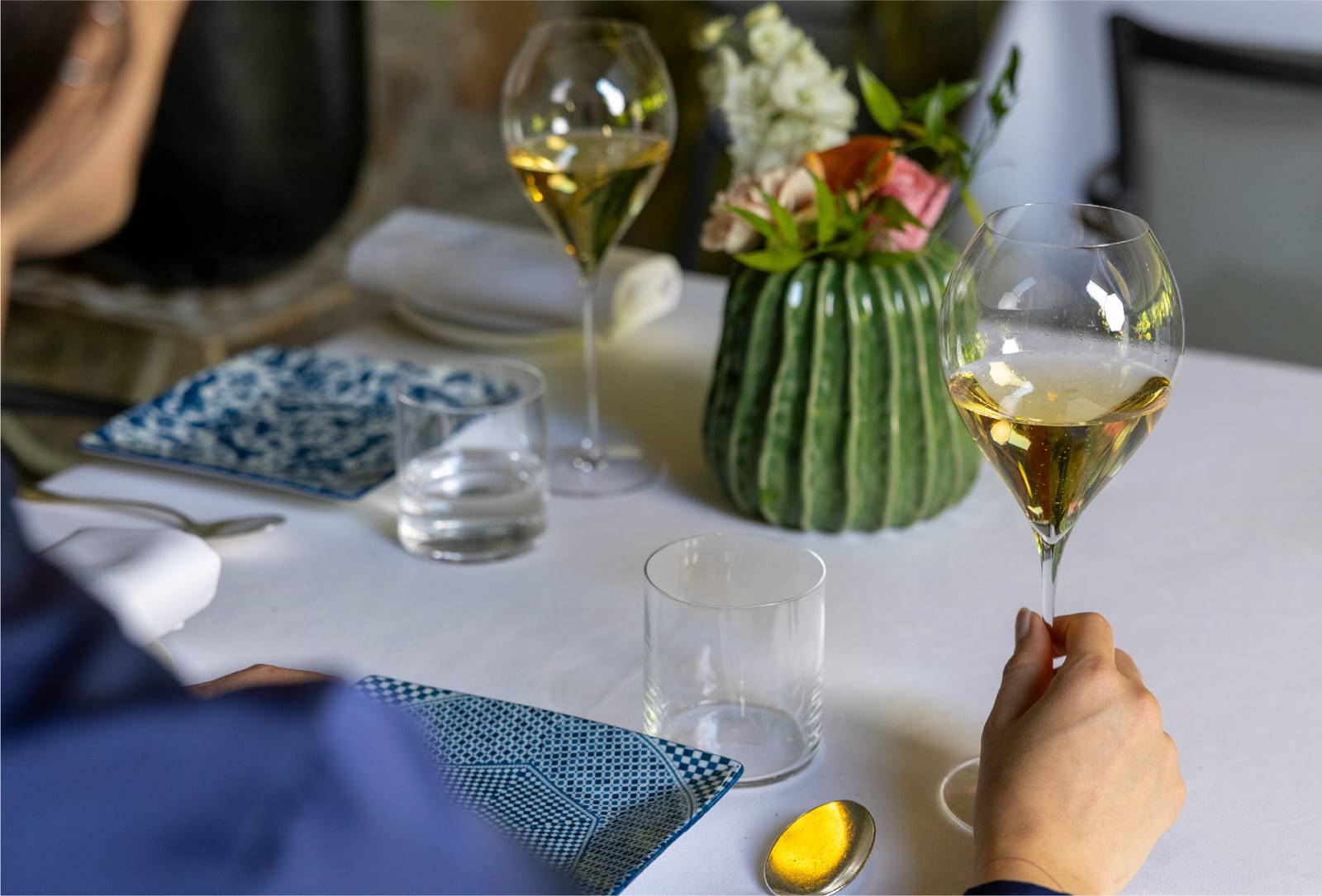 Tavola apparecchiata con calici di vino bianco e un vaso verde di fiori