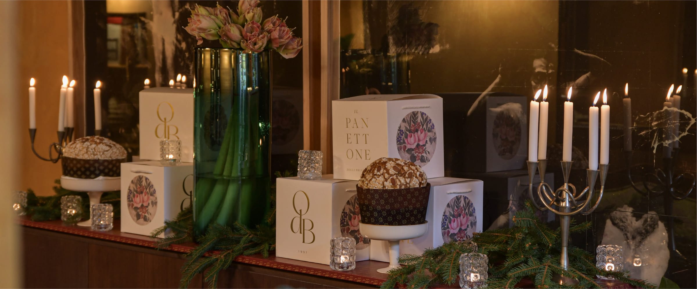 Credenza natalizia con panettoni su alzate, scatole con il monogramma OdB e candele accese