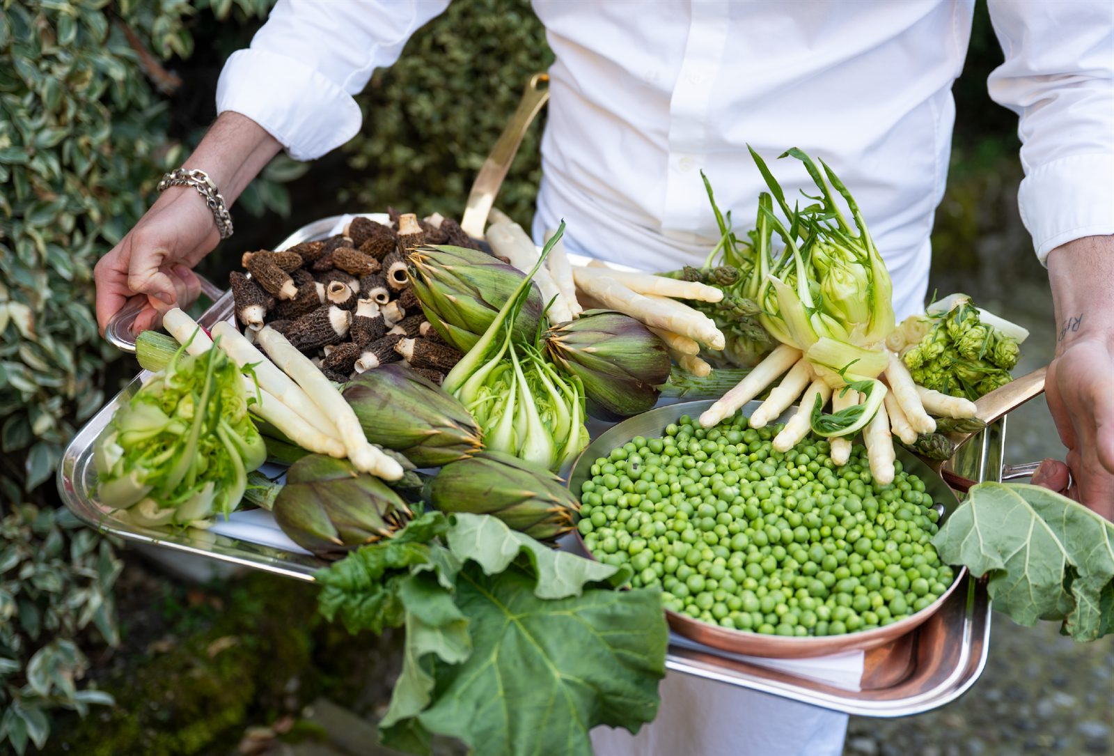 Lo chef Paolo Cortinovis regge un vassoio di verdure di stagione: spugnole, carciofi, asparagi bianchi e piselli